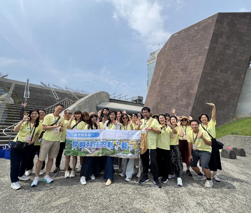 解謎完成，自然創藝組在十三行博物館前合影，舉起「穿越科技的創藝」旗幟，準備搭車前往下一站挖仔尾踏查。（照片提供者：新北市教育局 / 拍攝日期：2026.08.11）