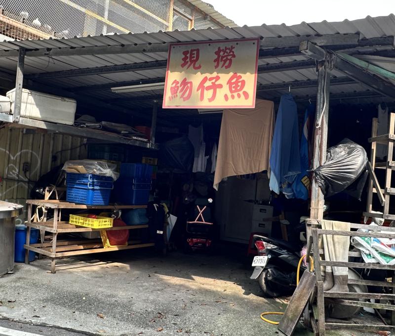 「現撈魩仔魚」招牌高掛在鐵皮棚下，漁具、籃筐與工作檯堆疊其間，是討海人家日常補給的作業空間，也是八里漁村最真實的生活切片。（照片提供者：郭庭禎 / 拍攝日期：2026.08.11）