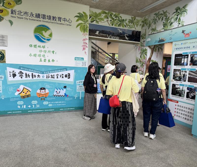 學員步入新北市永續環境教育中心，牆面寫著「保護地球，珍惜所有，永續環境，尊重生命」，一旁「淨零新動力」節能展區，引導大家思考日常減碳的行動。（照片提供者：許大偉 / 拍攝日期：2026.08.11）