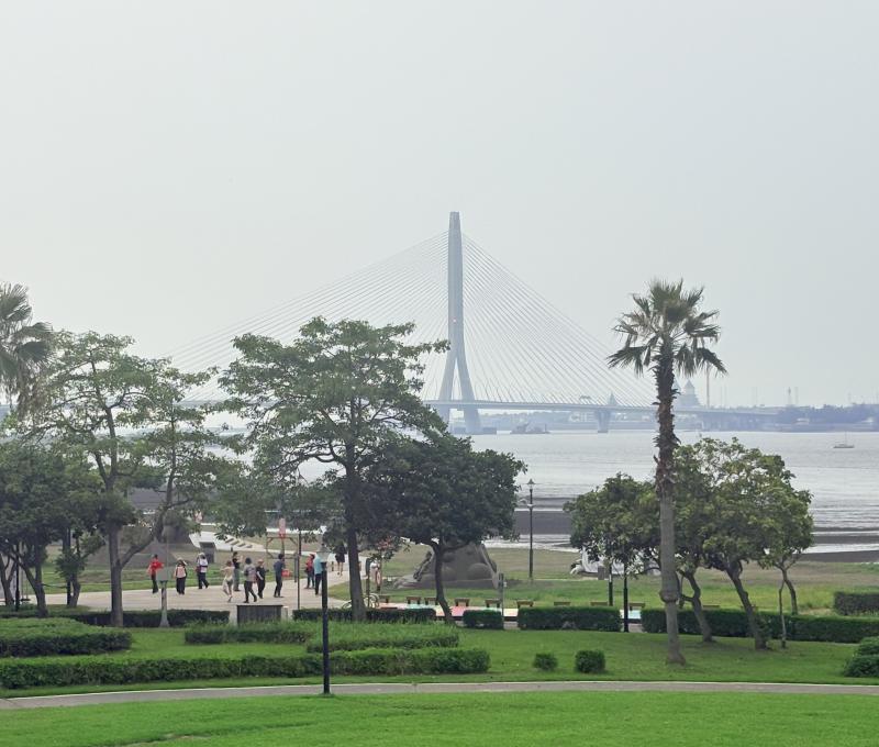 遠眺淡江大橋橫跨淡水河口，河岸綠意與城市景觀彼此交會。從八里的視角出發，看見自然、城市與人文共同交織的風景。（照片提供者：游子誼 / 拍攝日期：2026.08.11）