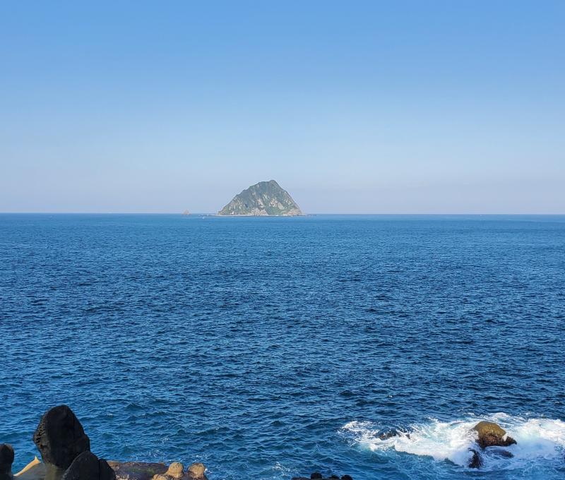 眺望青空與湛藍海面的交界，可見基隆嶼靜靜矗立著。拍攝者：王懷璿∕拍攝日期：2025/12/16