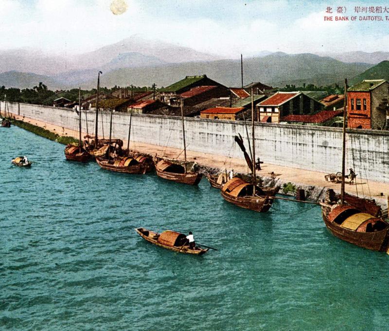 大稻埕的鋼筋混凝土牆式堤防與牧彥七時代的間知石砌低水護岸堤防皆位於第一代臺北橋的北側，但結構上已大不相同。資料來源：〈臺北市大稻埕河岸〉（約1920年代），國家圖書館典藏。